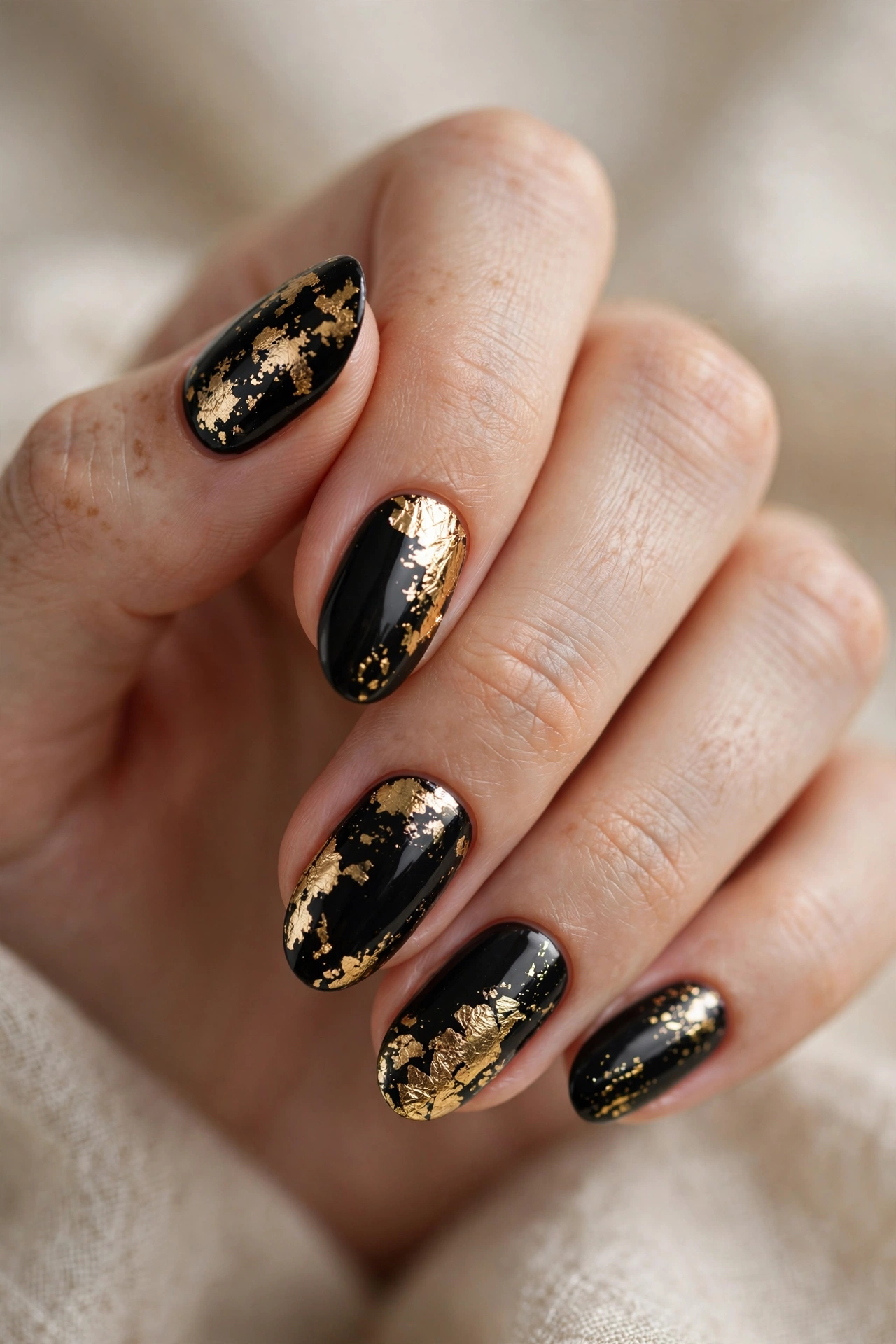 Black and gold nail designs with metallic foil accents on dark glossy nails